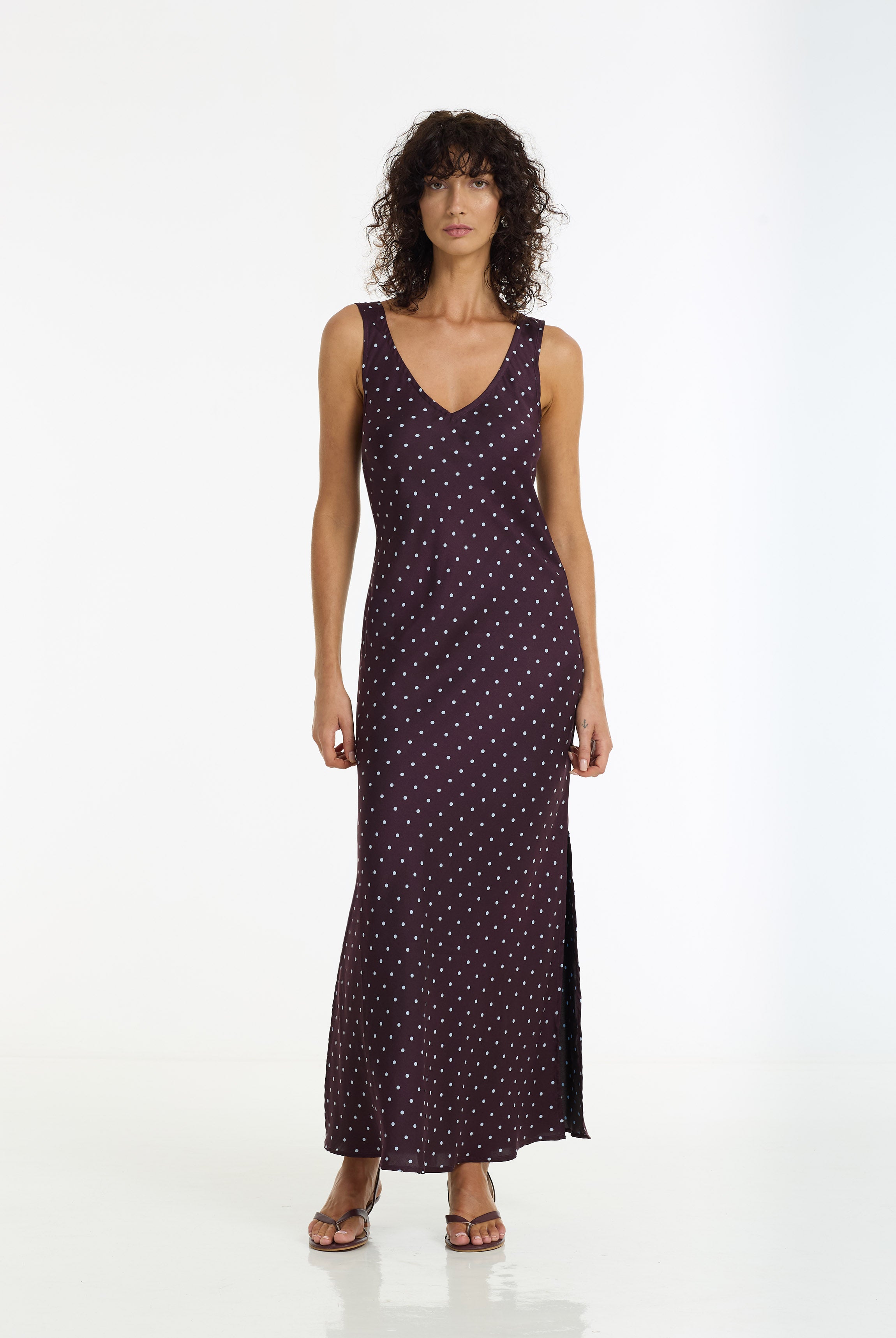 A woman modeling a Alexandria Spot Bias Cut Maxi Dress in burgundy by BLAK, standing against a plain white studio background.