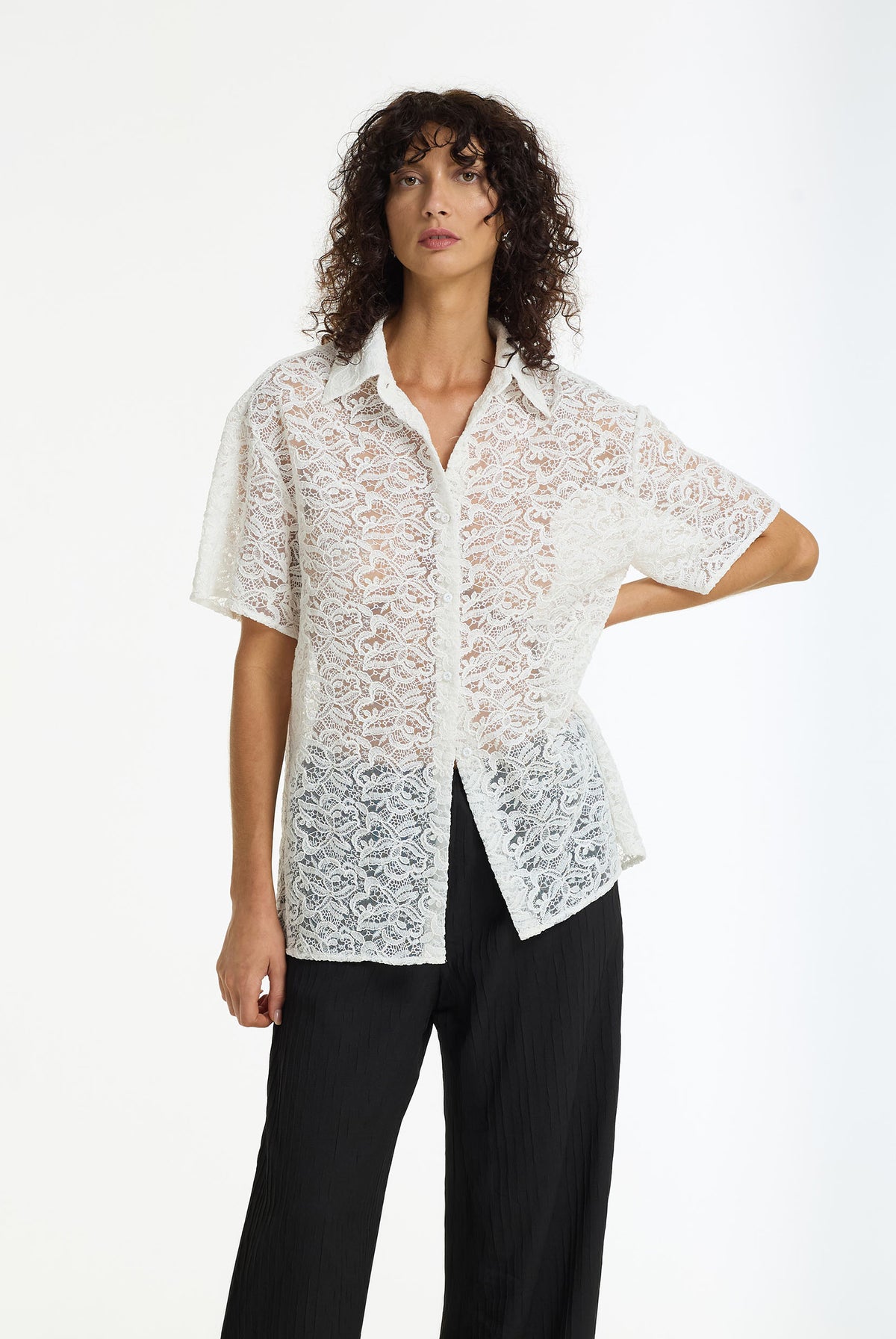 A model wearing the Align Short Sleeve Lace Shirt in white by BLAK, paired with black wide-leg trousers, against a plain white studio background.