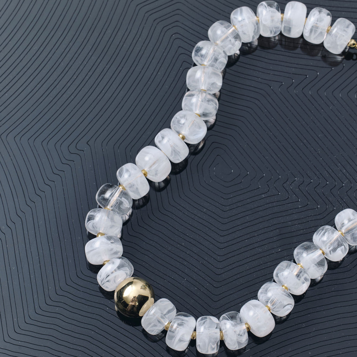 A beaded necklace made of faceted, translucent white beads with a single metallic gold accent bead, displayed on a dark textured background.