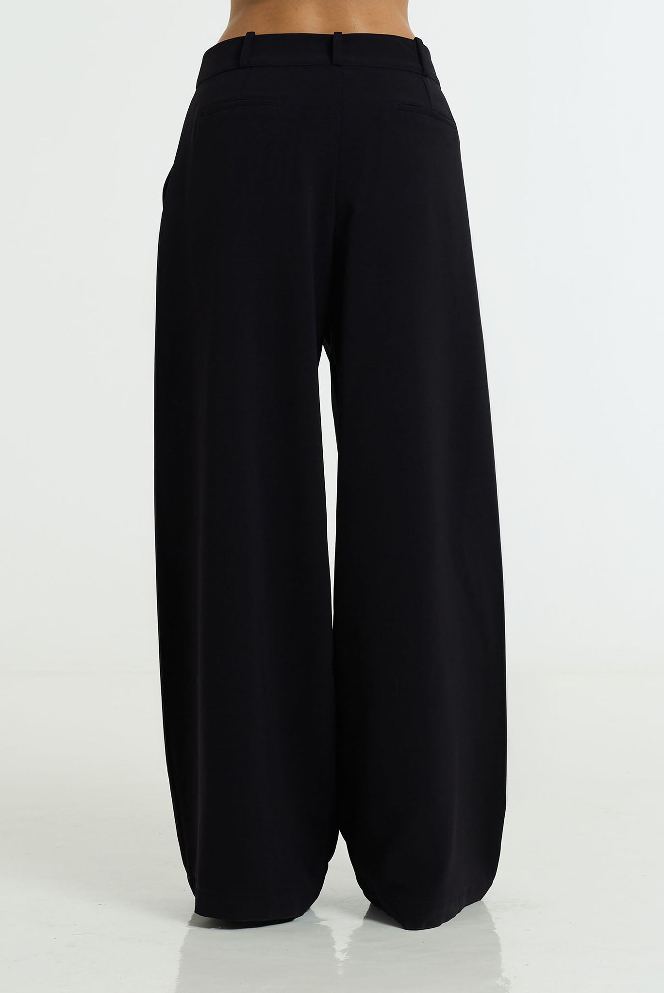 Black wide-leg trousers shown from the back on a model, featuring a high waistband and a relaxed, voluminous silhouette.