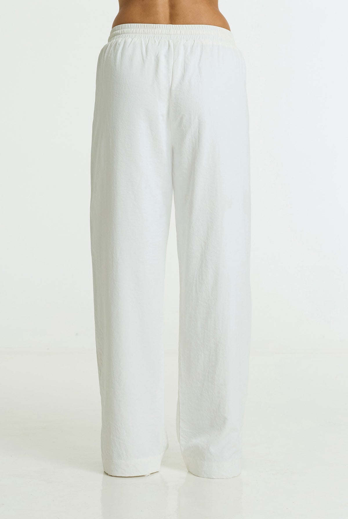 White wide-leg lounge pants shown from the back on a model, featuring an elastic waistband and a relaxed straight-leg fit.