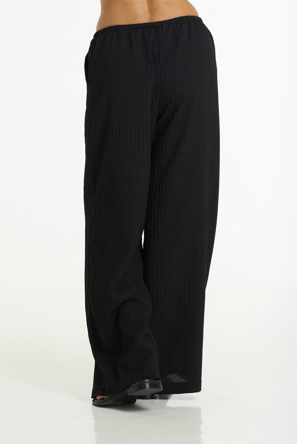Black wide-leg trousers with a subtle vertical textured stripe pattern, shown from the back on a model against a white studio background.