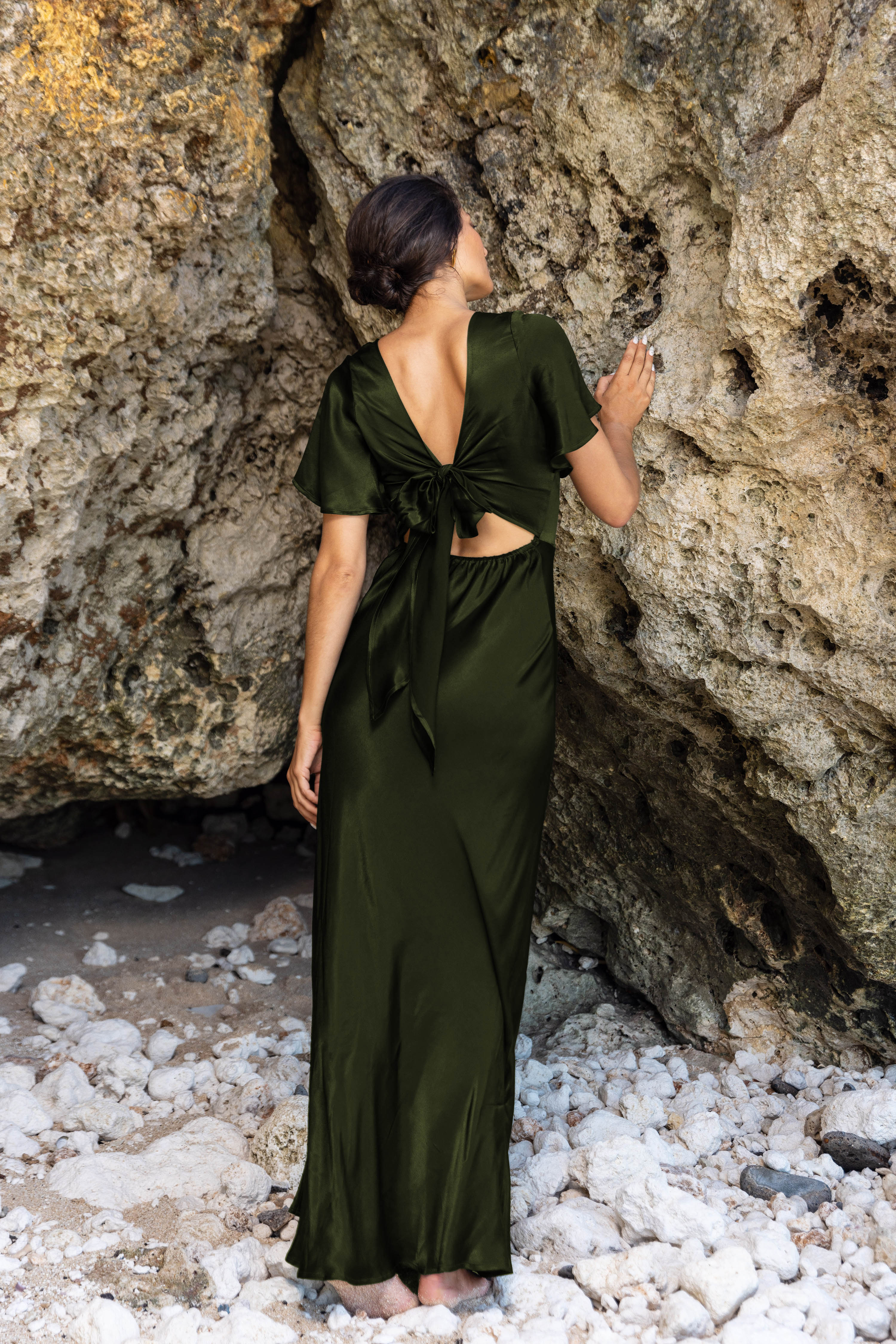 Woman in a green dress standing by a rocky wall.