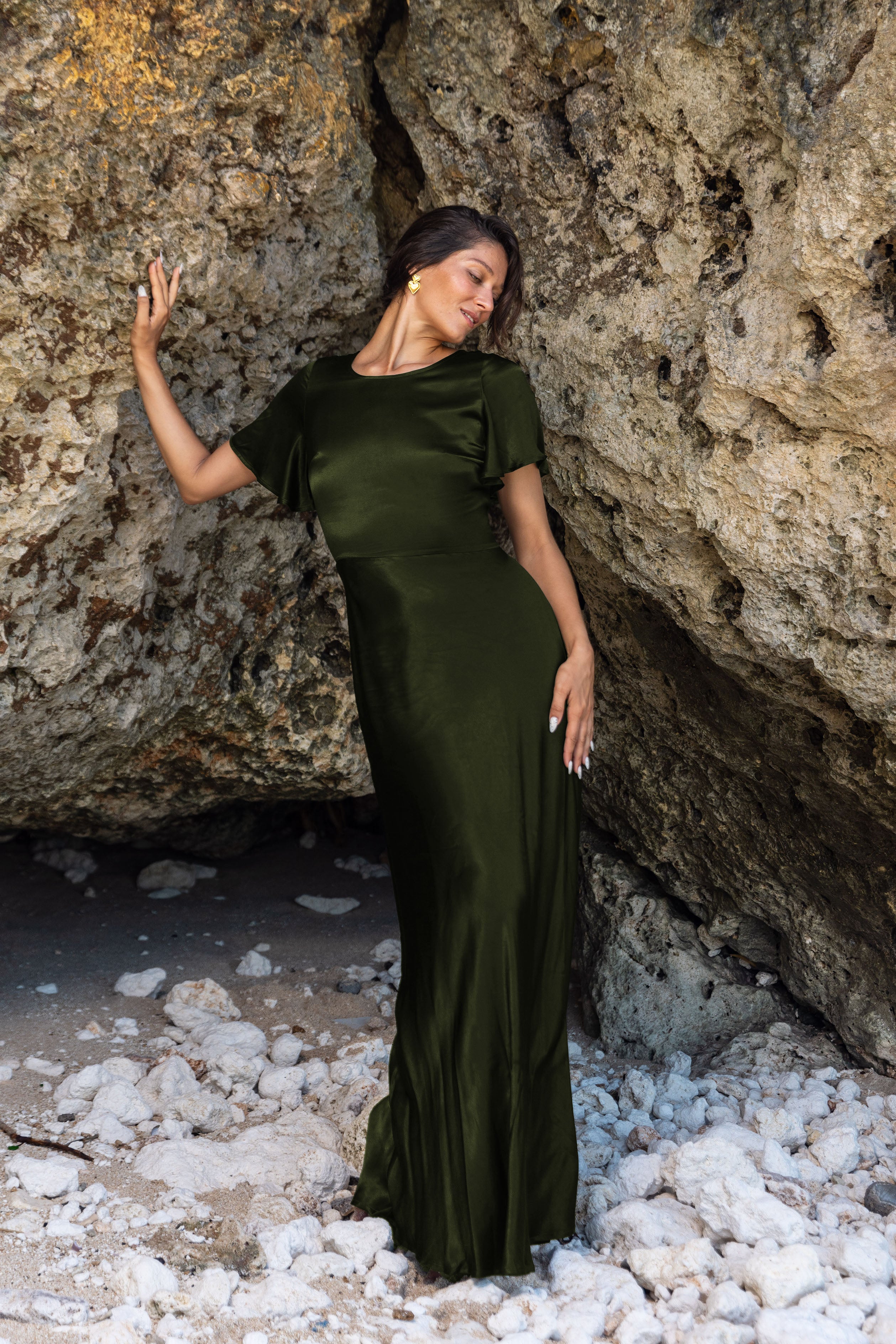 Woman in a dark green dress standing in a rocky cave.
