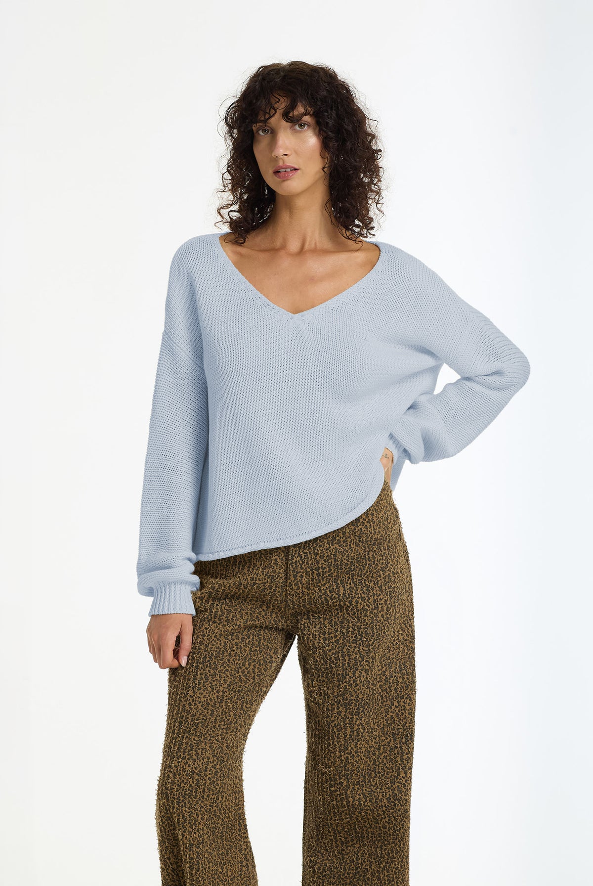 A woman modeling a Keep Me Close Cotton Yarn Sweater in Becky Blue by BLAK, paired with brown textured knit pants, against a plain white studio background.