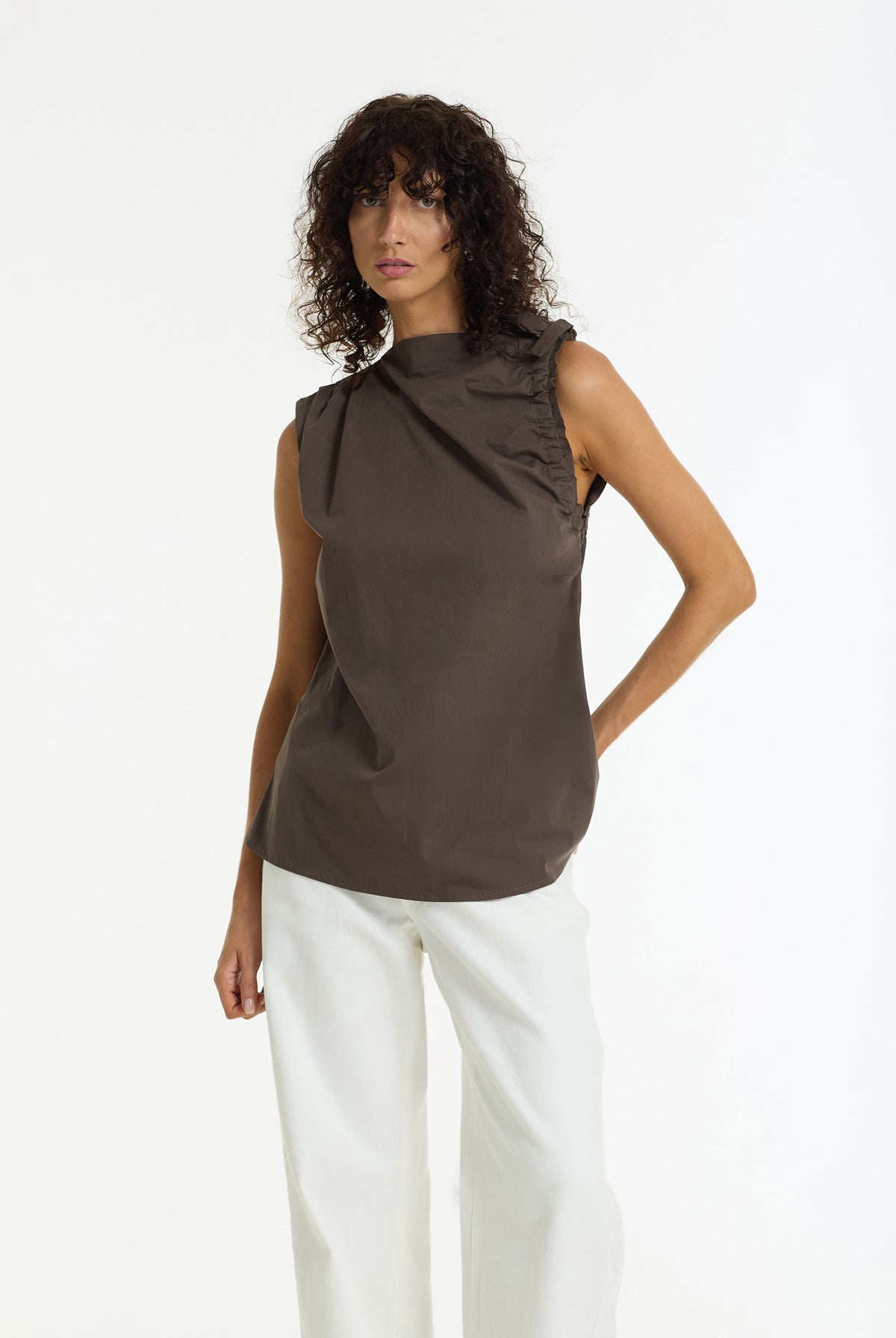A model wearing a Last Breath Sleeveless Cotton Top in Choc Stone by BLAK, paired with white wide-leg trousers, against a plain white studio background.
