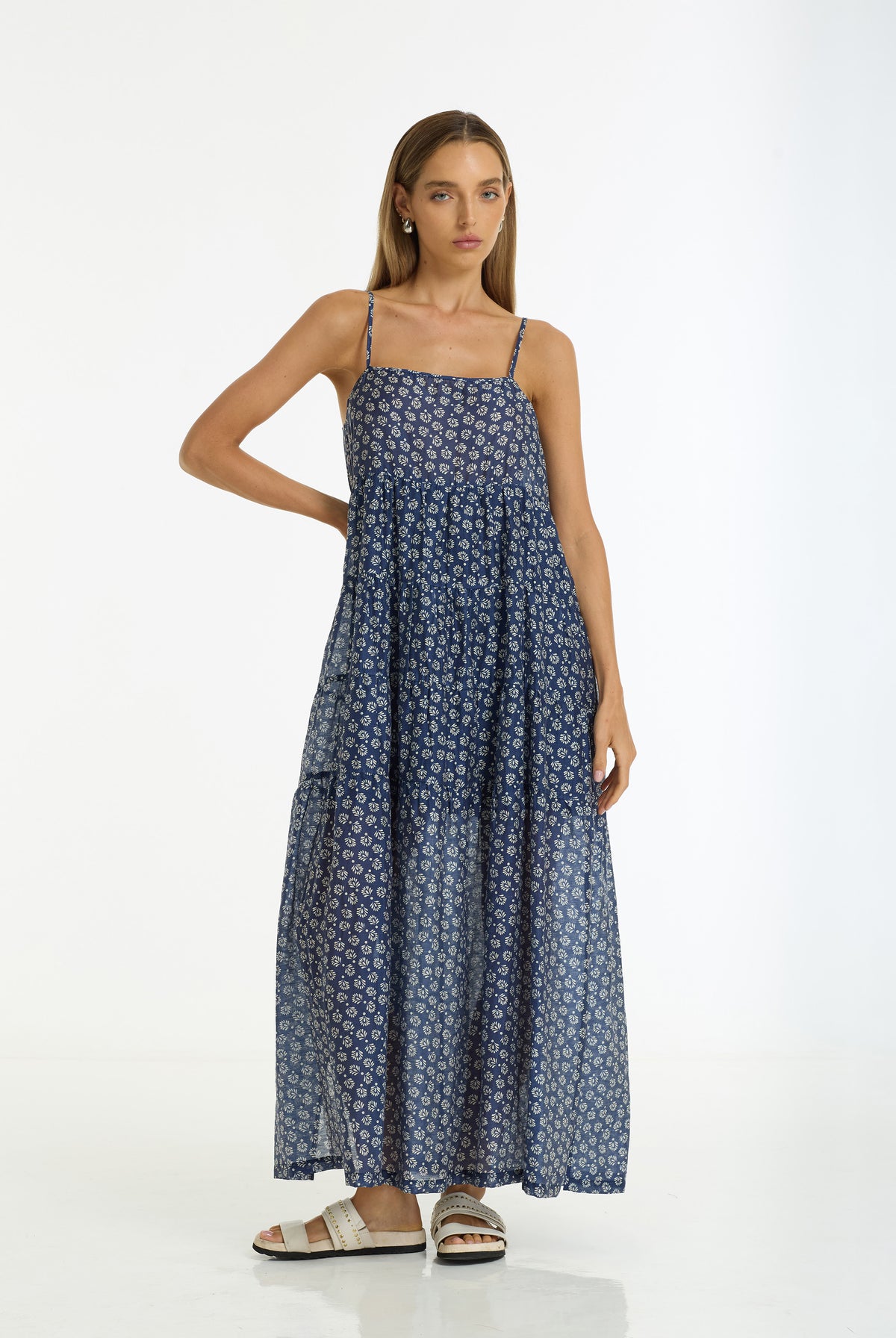 A woman modeling a Carmen Floral Print Maxi Dress in navy by BLAK, paired with beige slide sandals, against a plain white studio background.
