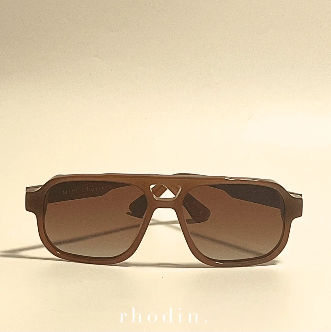 Brown sunglasses on a beige background with 'rhodin' branding.