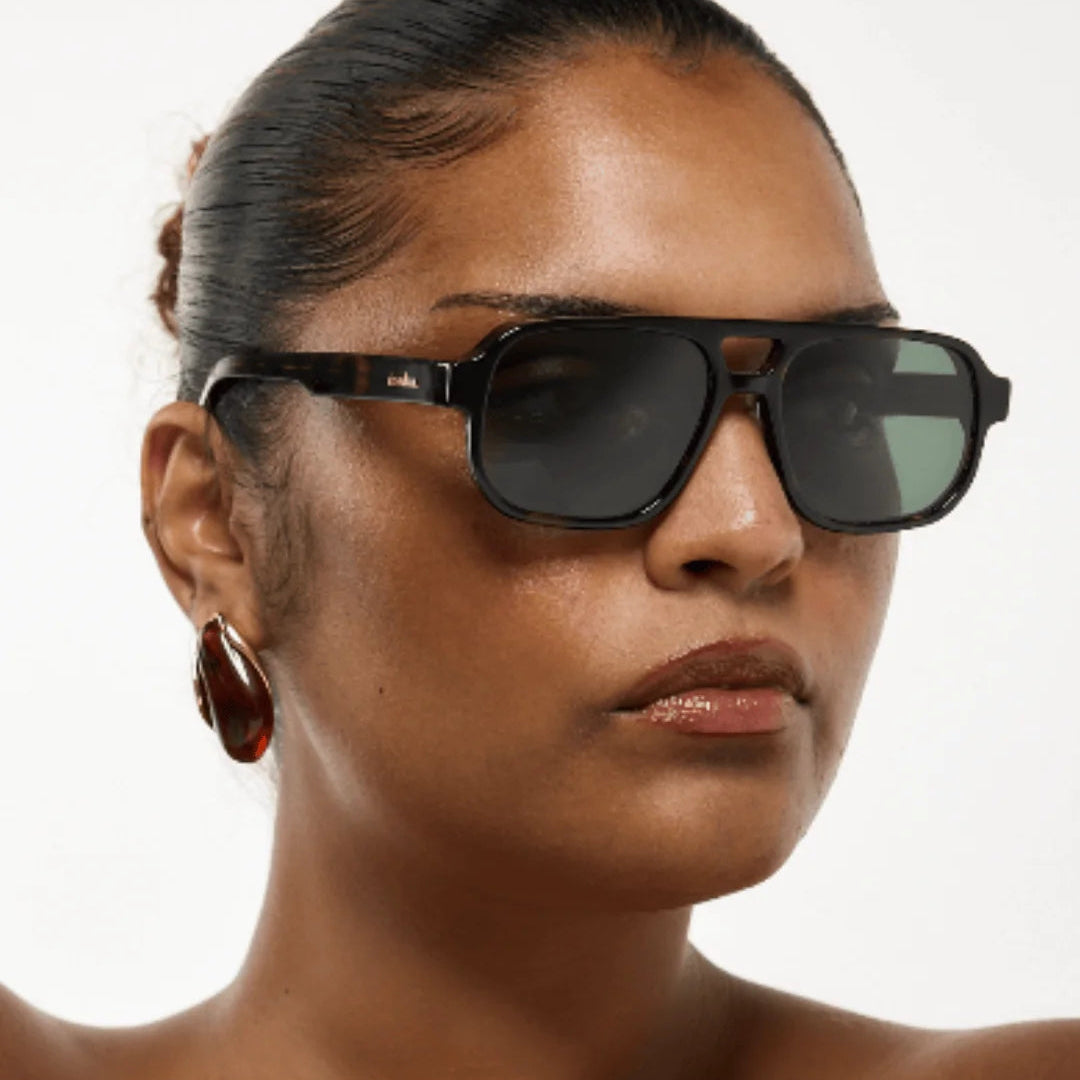 Woman wearing dark sunglasses with a plain background
