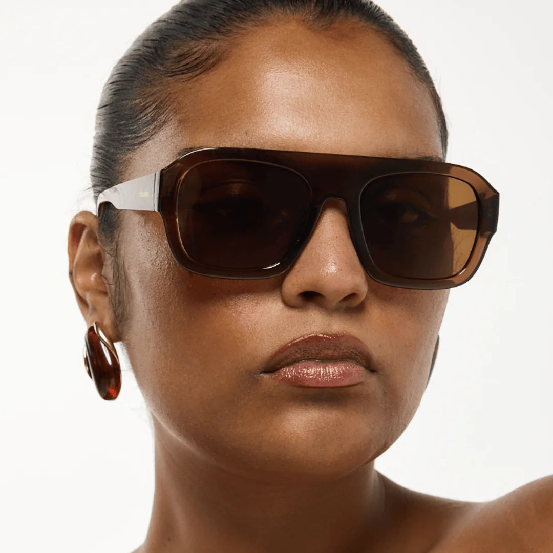 Woman wearing brown sunglasses with a plain background, featuring the brand 'rhodin'.