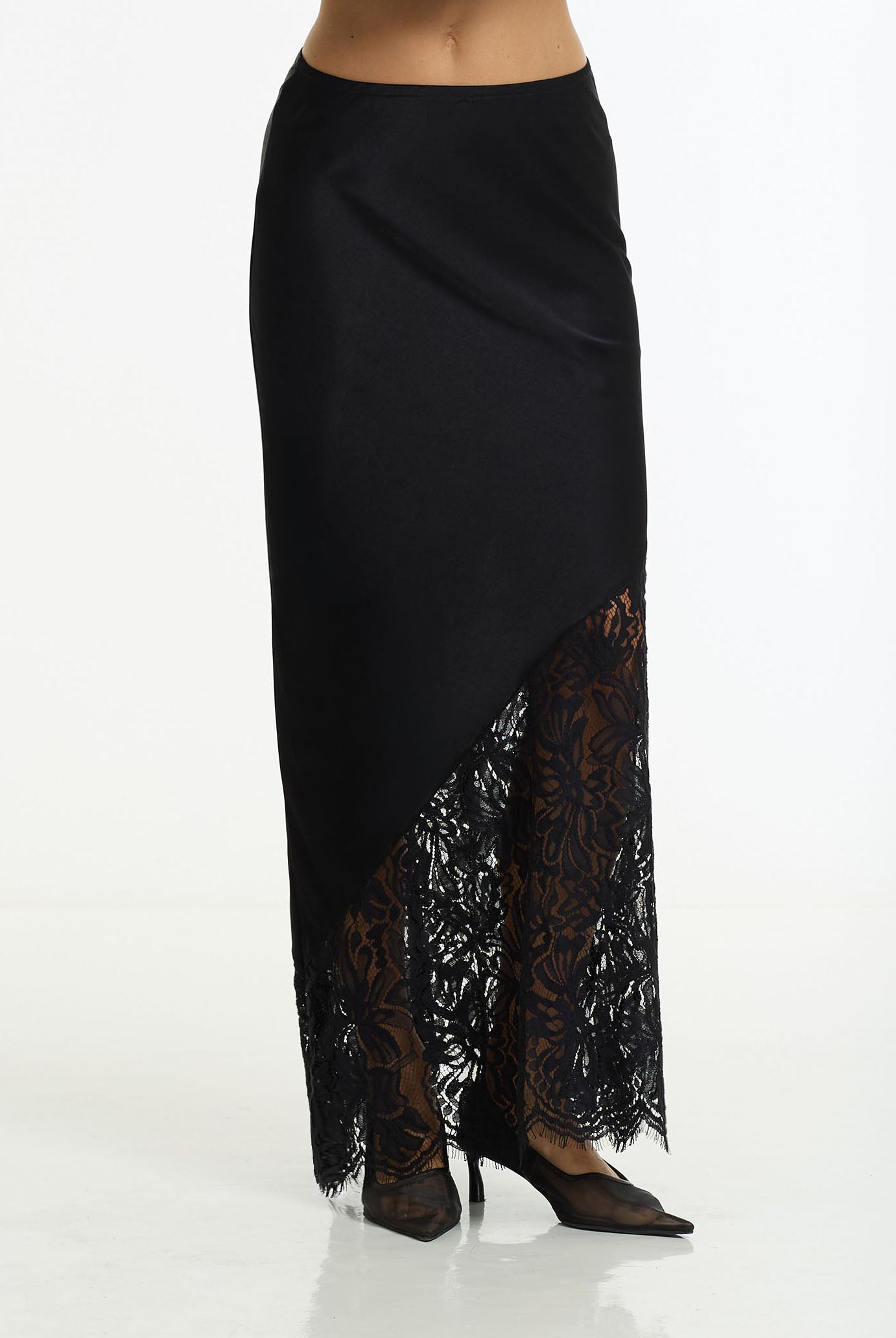 A black bias maxi skirt with a diagonal sheer lace panel at the hem, shown on a model against a plain white studio background.