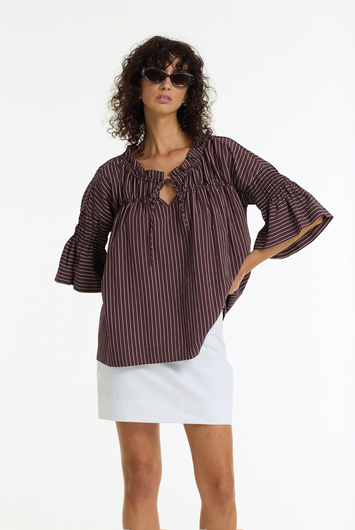 A model wearing a wine and white vertically striped, flared three-quarter sleeve top with a keyhole cutout, paired with a white skirt, against a plain white background.