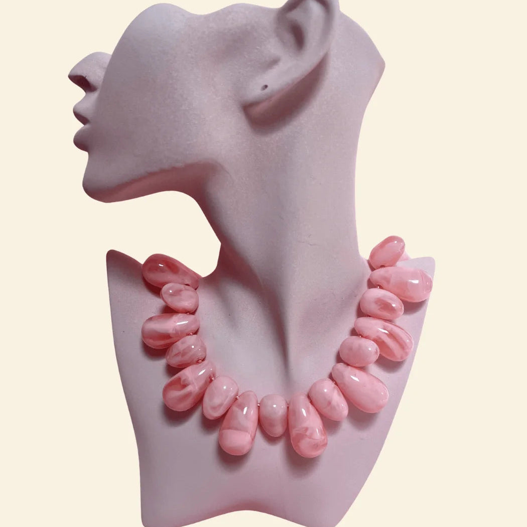 A pink beaded necklace displayed on a pale pink mannequin bust against a light cream background, with the brand name rhodin. printed below.