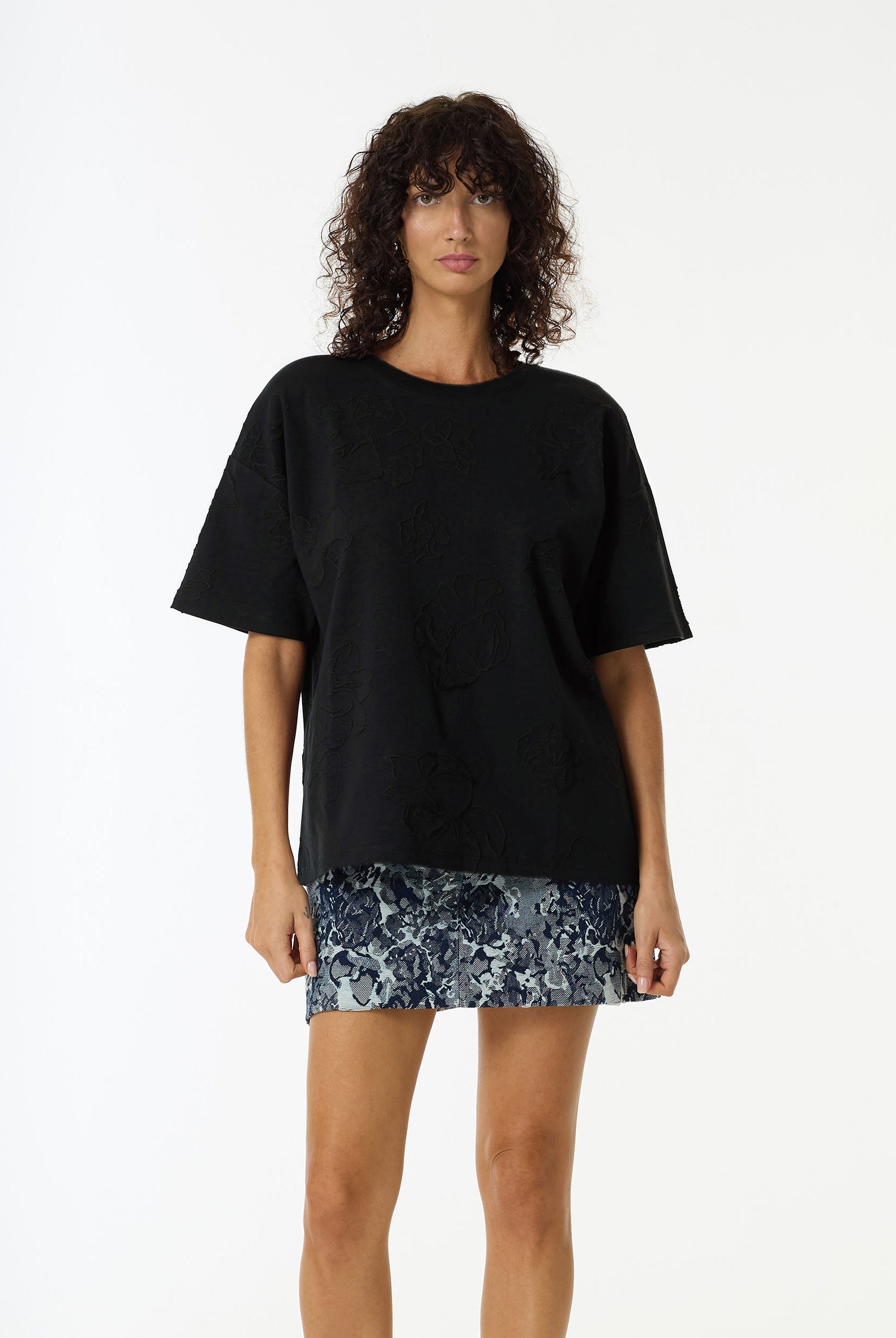 Woman wearing the Off Duty Flora Textured Tee in Black by BLAK and a floral mini skirt on a white background