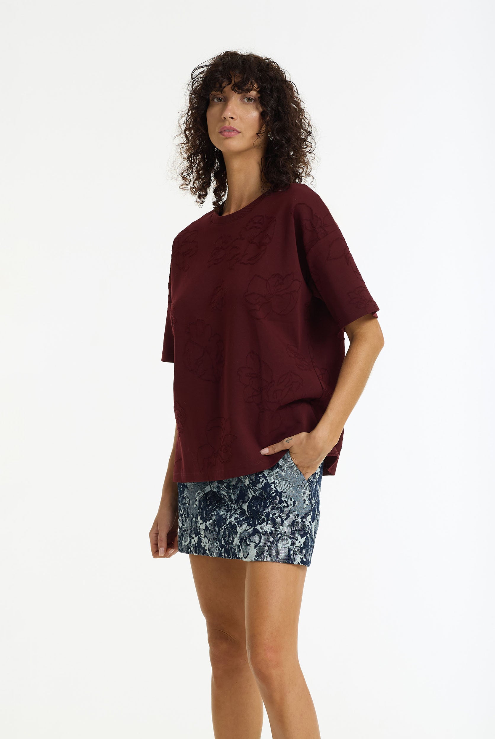 Woman wearing a burgundy oversized top and floral mini on a white background