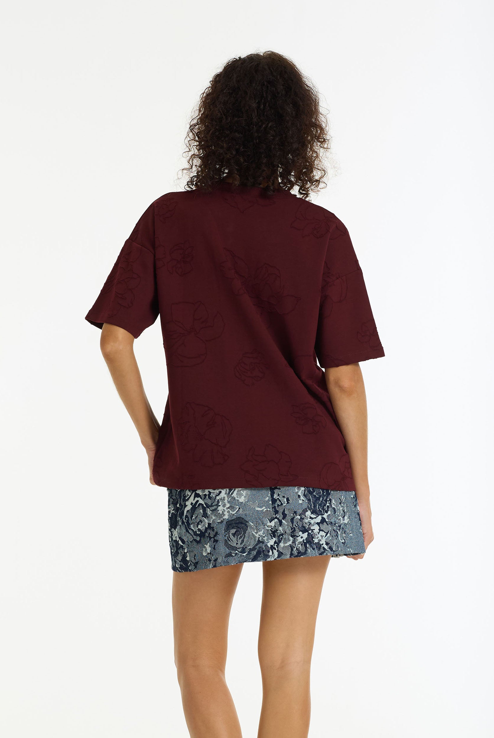 Person wearing a burgundy oversized t-shirt and floral skirt on a white background