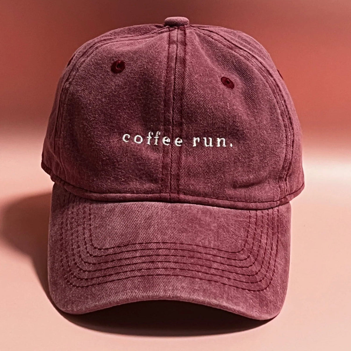 Maroon cap with 'coffee run' text on a pink background
