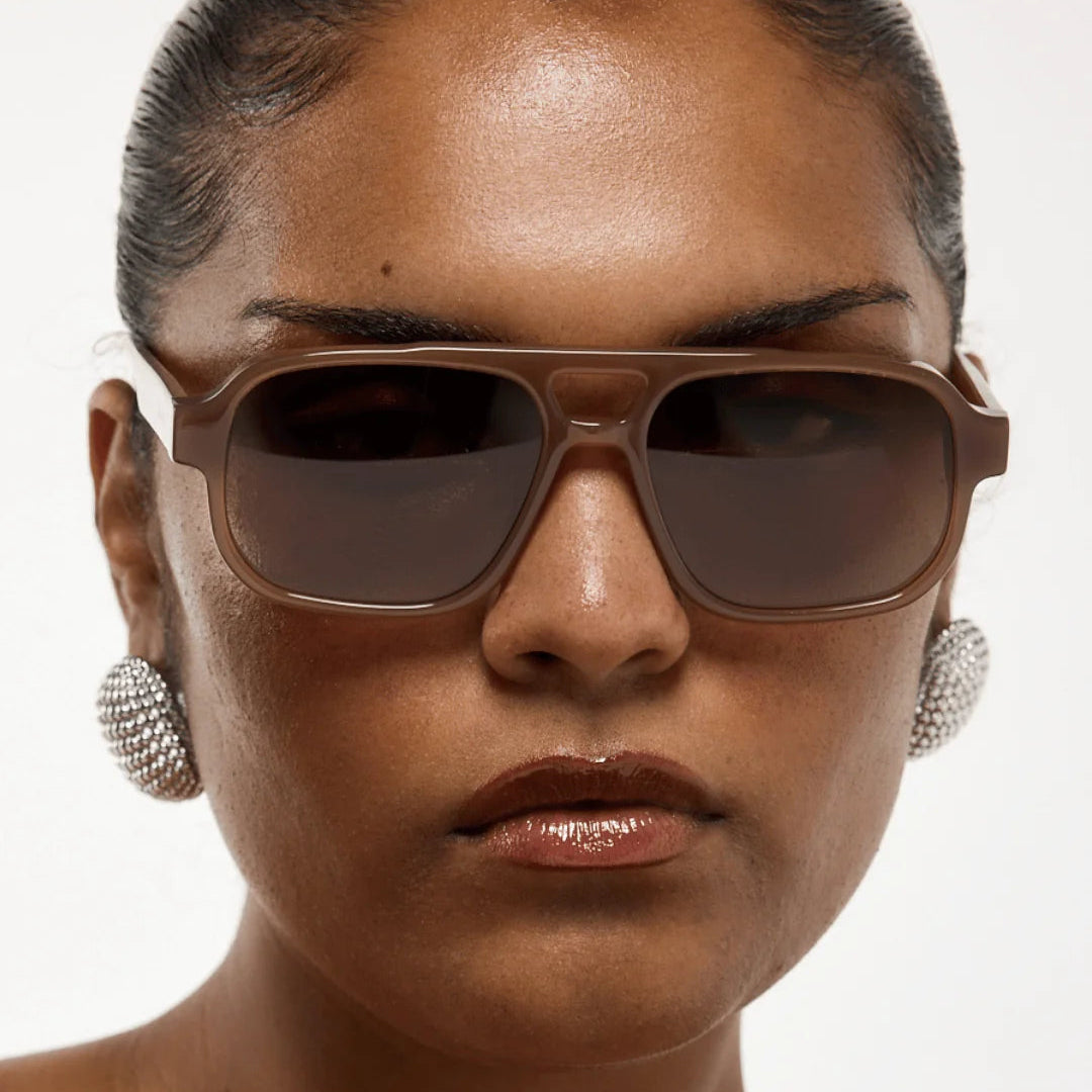 Woman wearing brown sunglasses with a plain background, featuring the brand 'rhodin'.