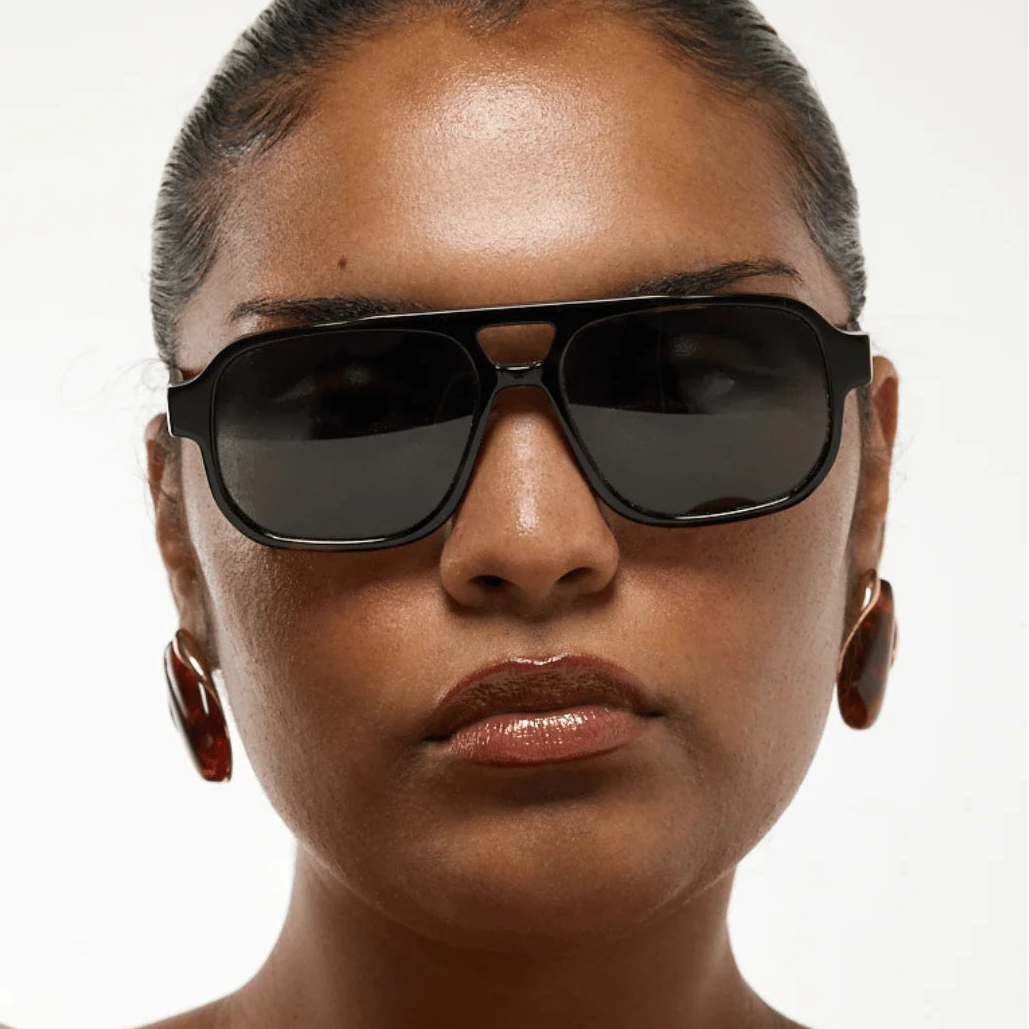 Woman wearing dark sunglasses against a white background
