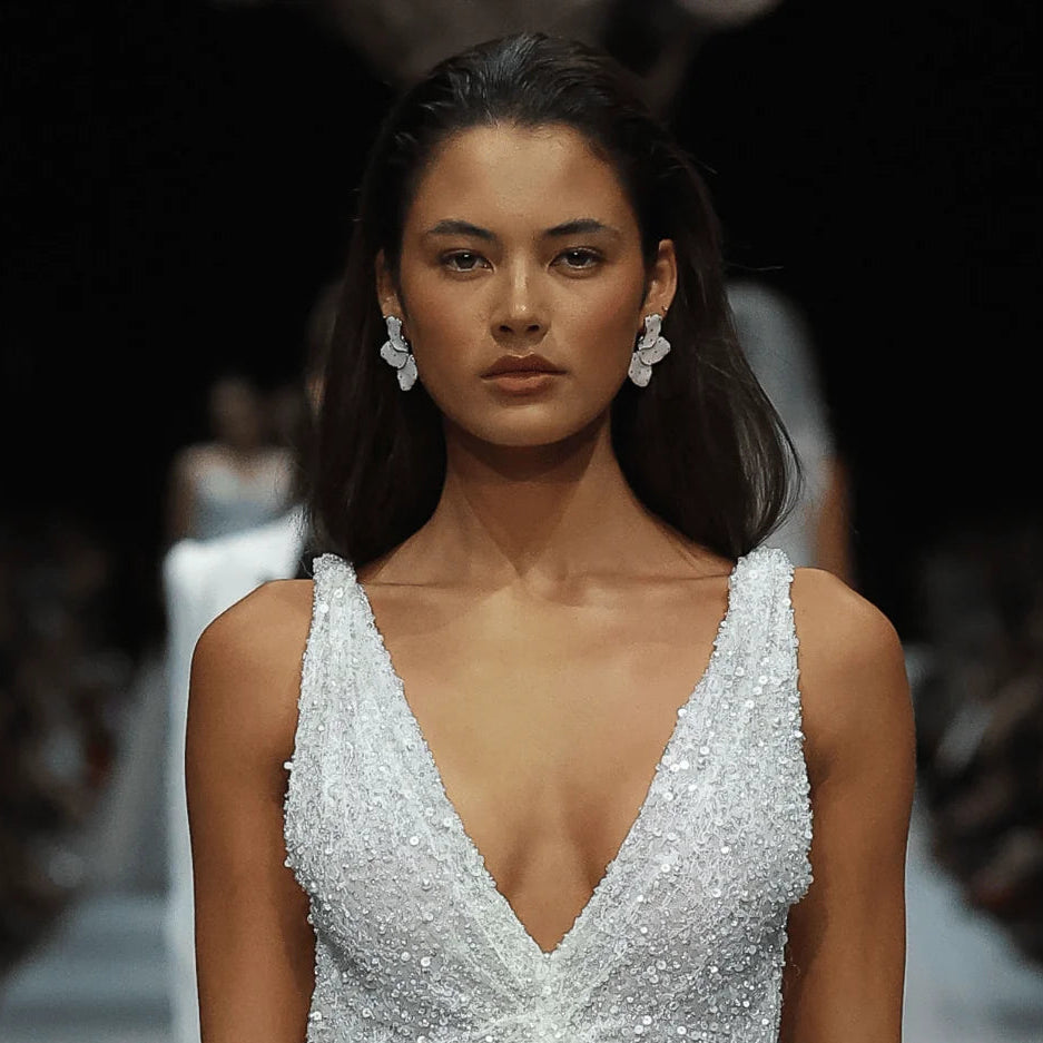 Model wearing a sparkling silver gown with floral details on a runway, brand 'rhodi' visible.