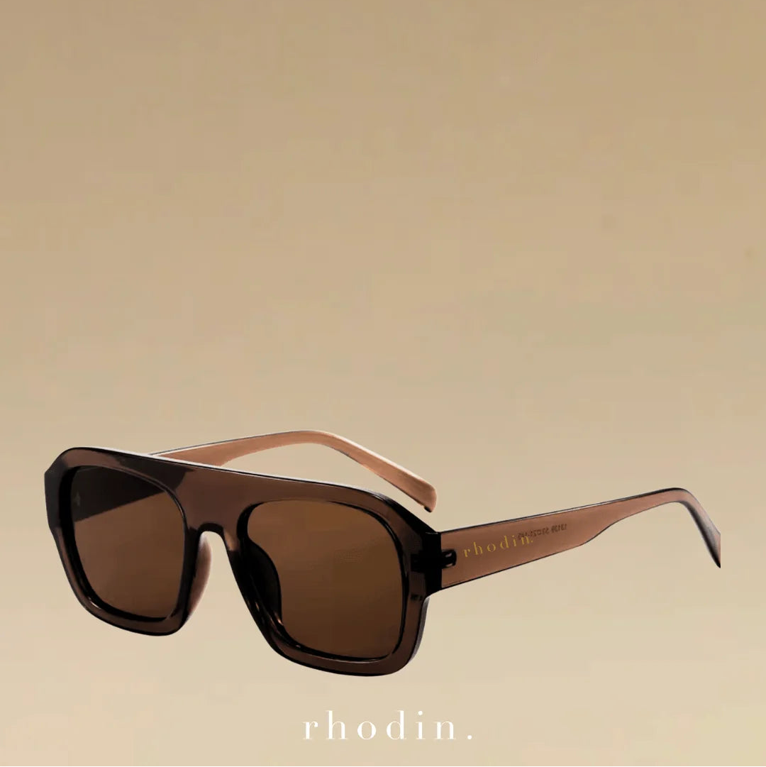 Rhodin oversized square sunglasses with dark brown lenses, a translucent dark brown acetate frame, and light brown temples, shown on a solid beige background.