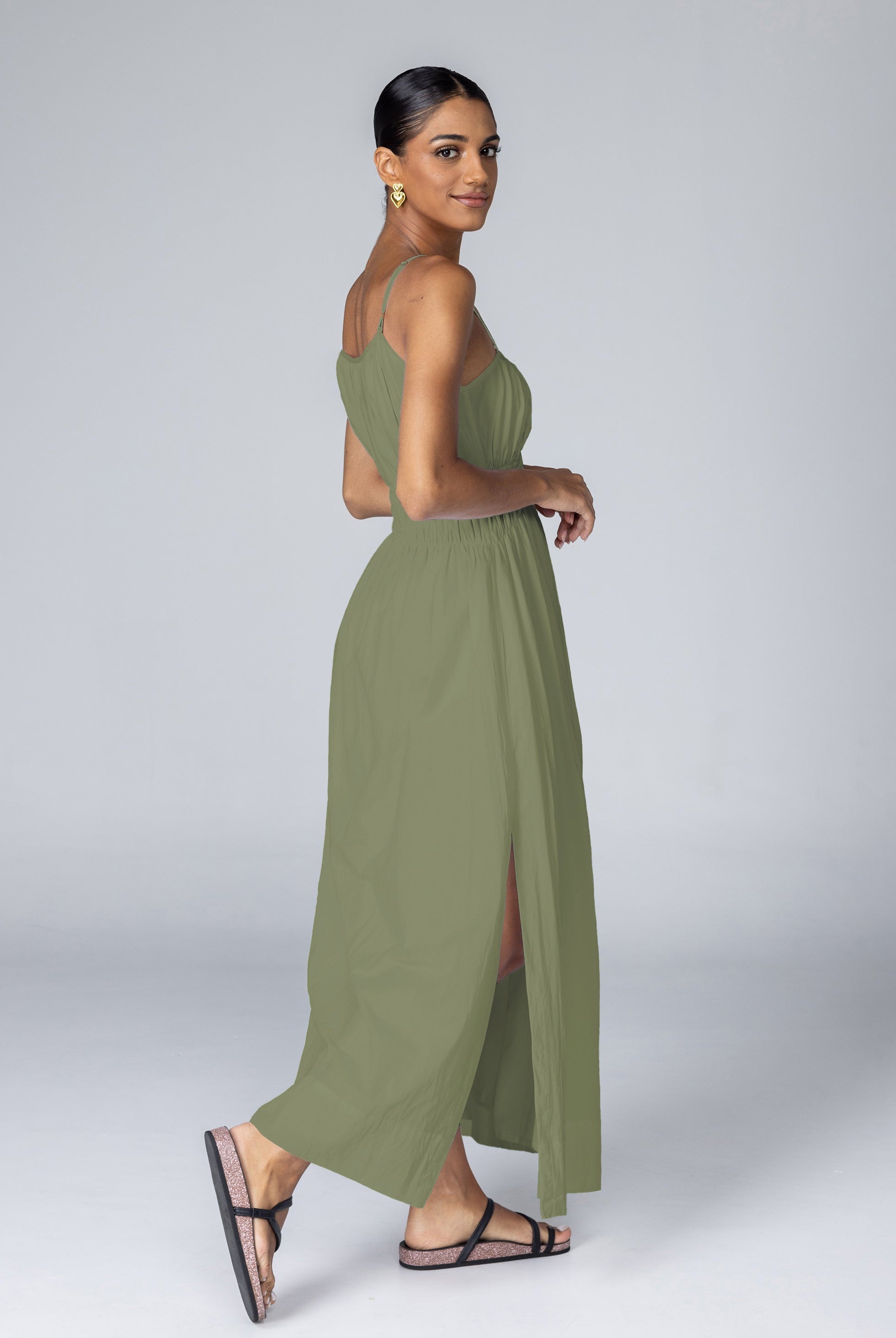Woman wearing a green dress with a slit on a plain background
