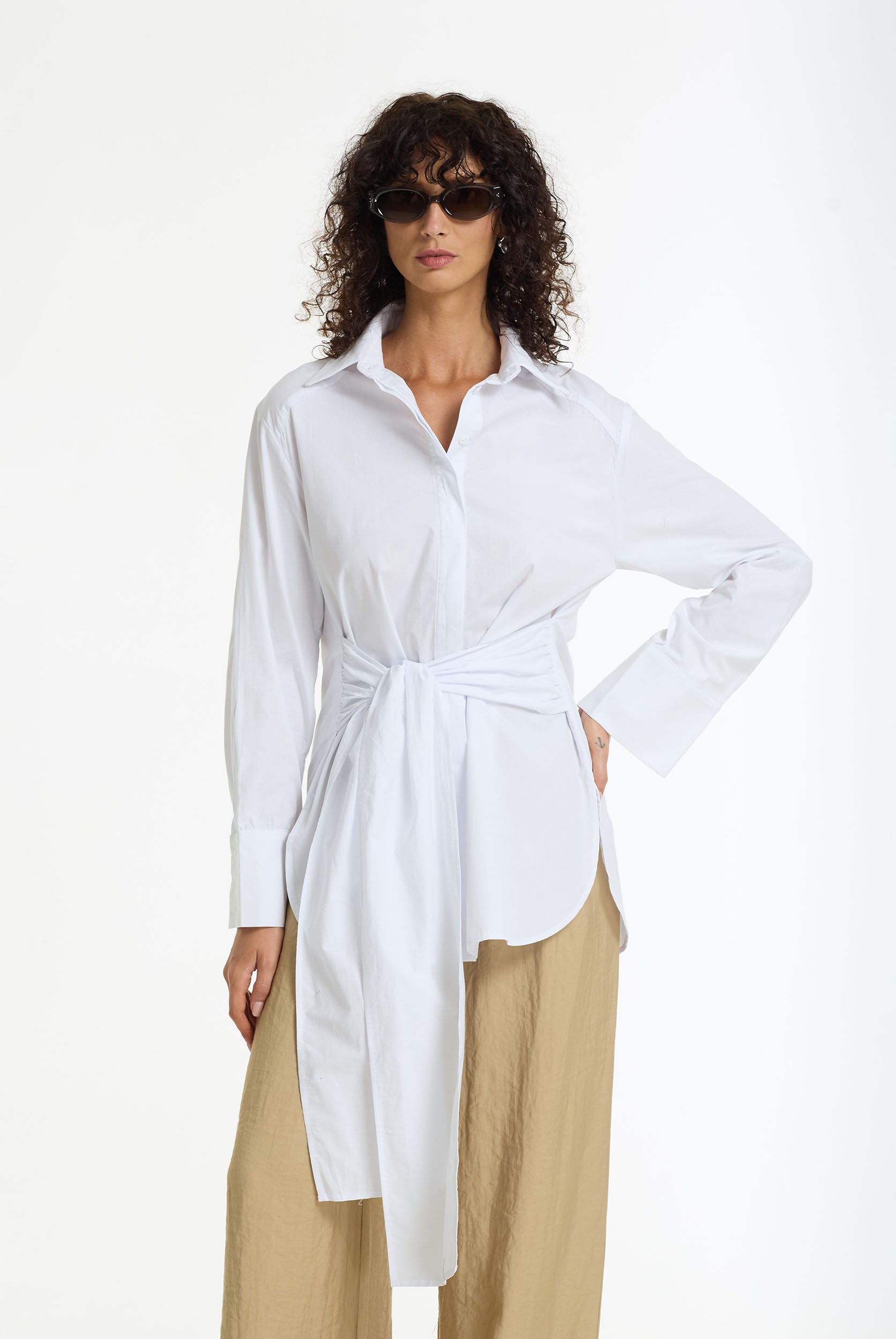 Woman wearing the Something About You Tie Waist Cotton Shirt in White by BLAK and beige wide leg pants on a white background
