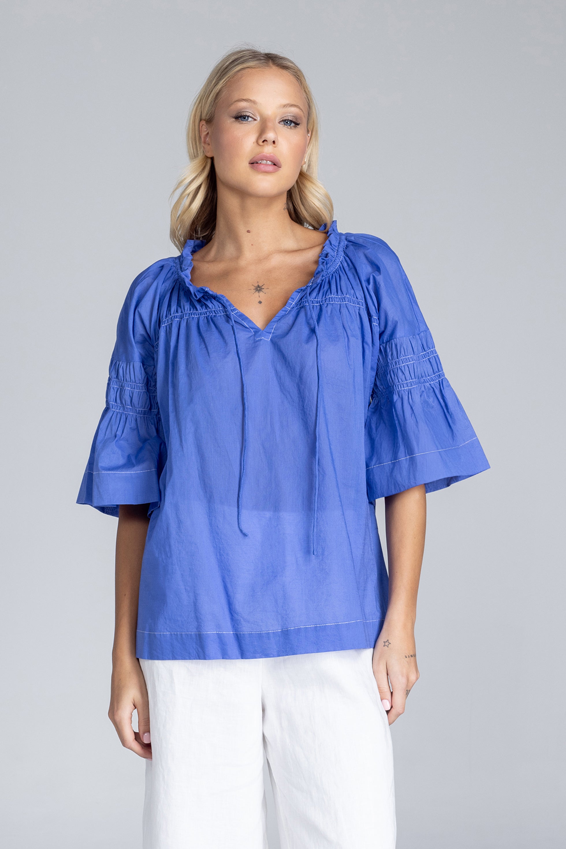 Woman wearing a blue blouse with white pants on a gray background