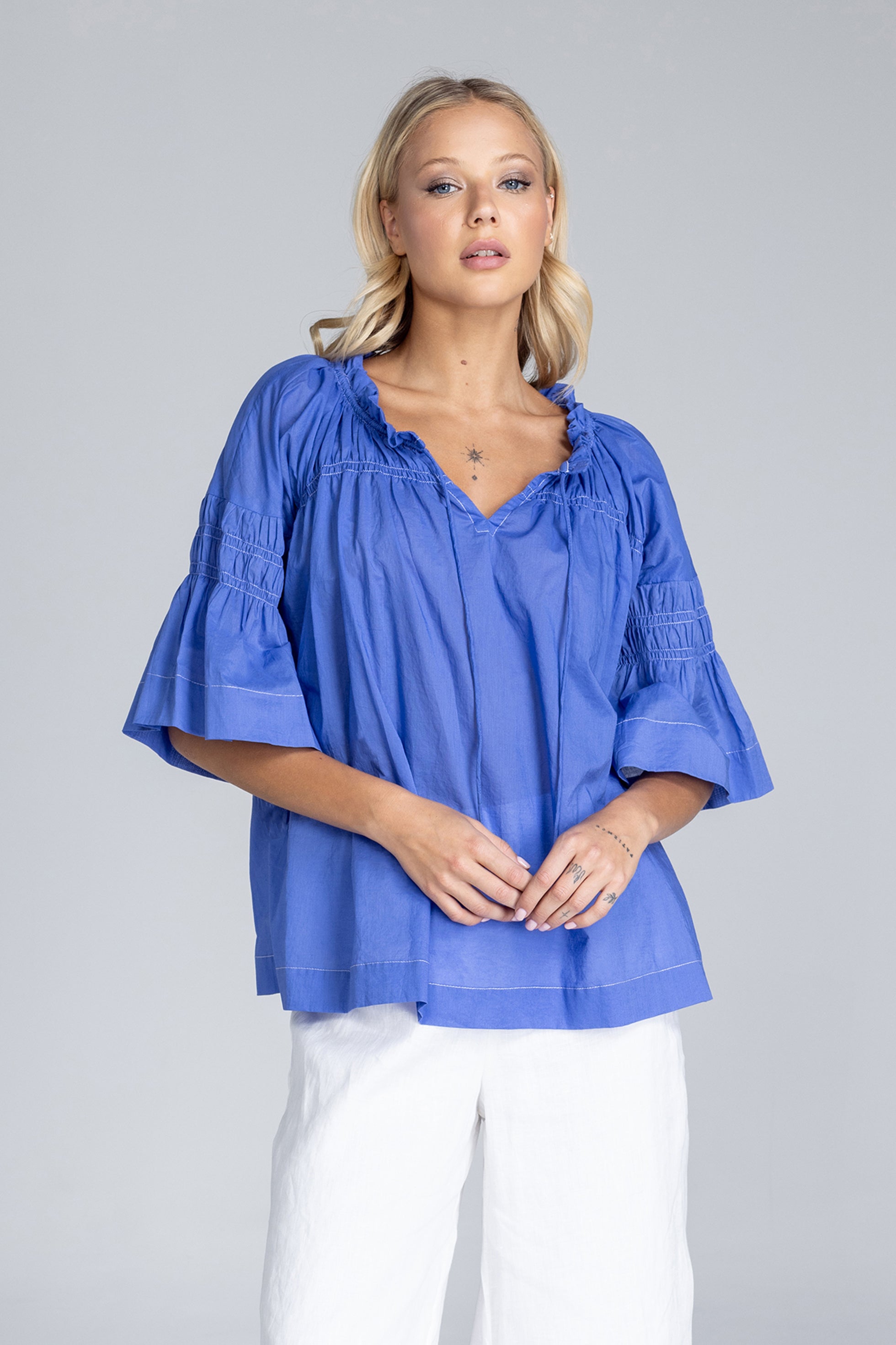 Woman wearing a blue blouse with ruffled sleeves on a gray background