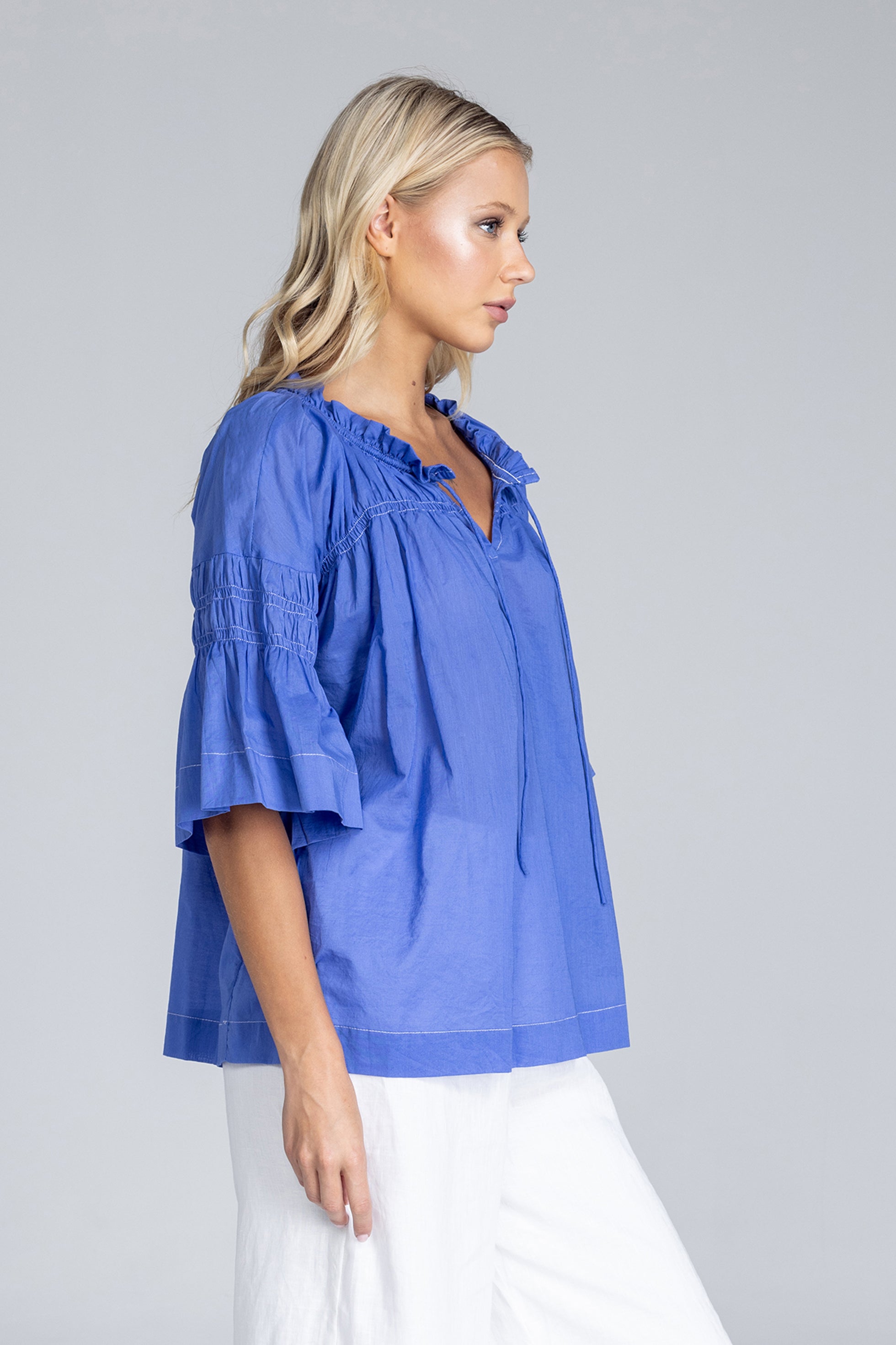 Woman wearing a blue blouse with ruffled sleeves on a gray background