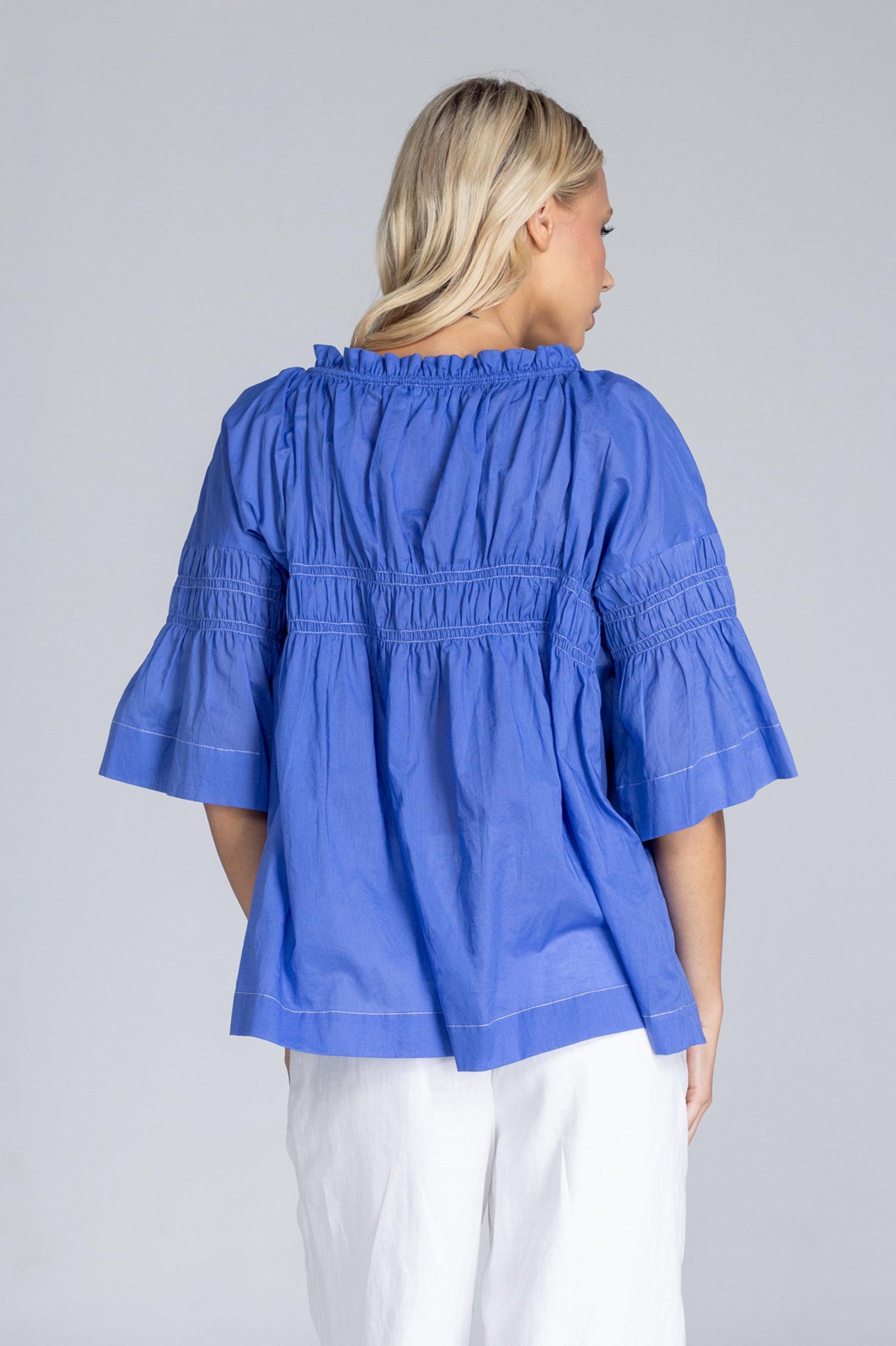Woman wearing a blue blouse with ruffled sleeves on a gray background