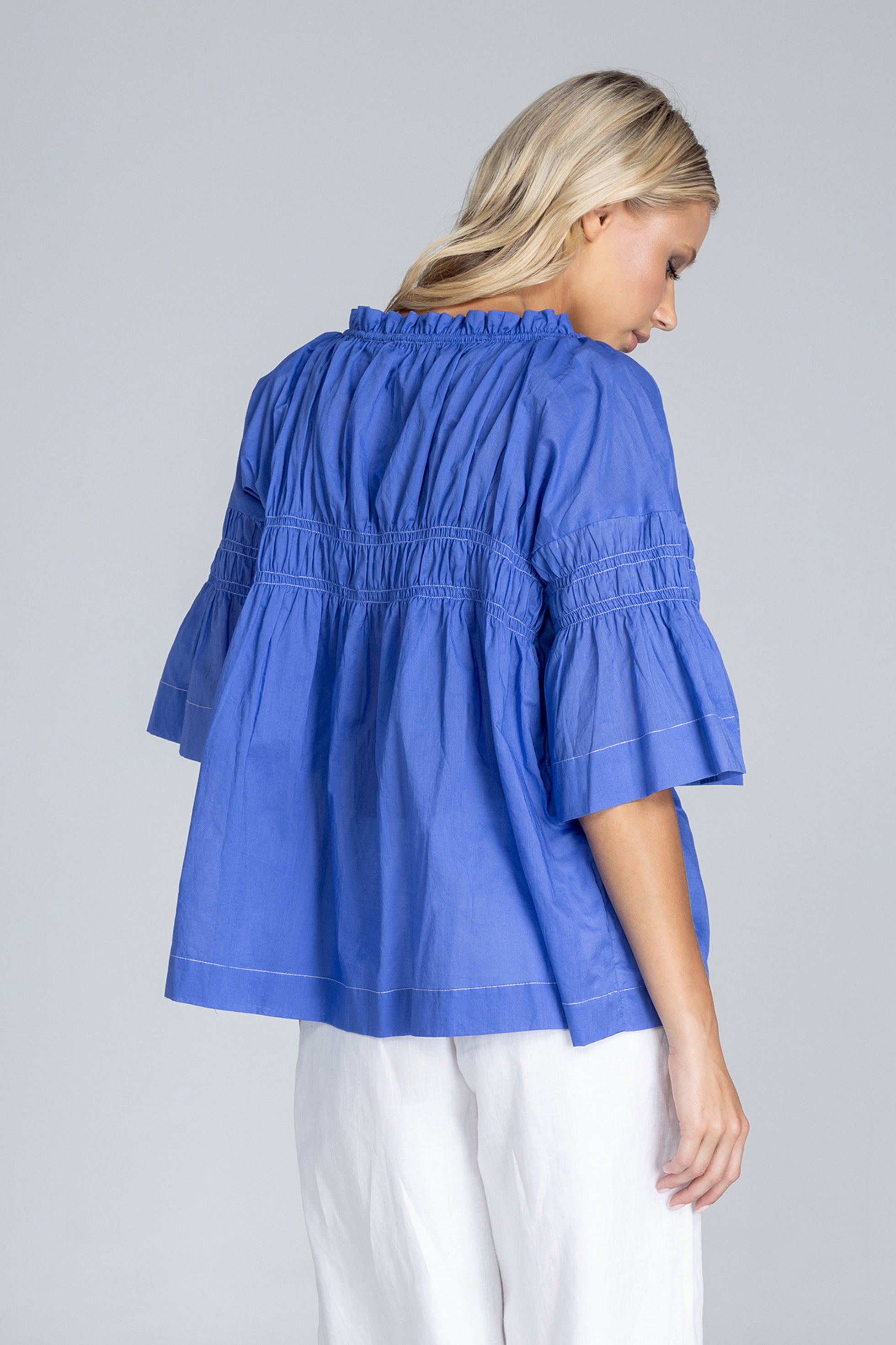 Woman wearing a blue blouse with ruffled details on a gray background