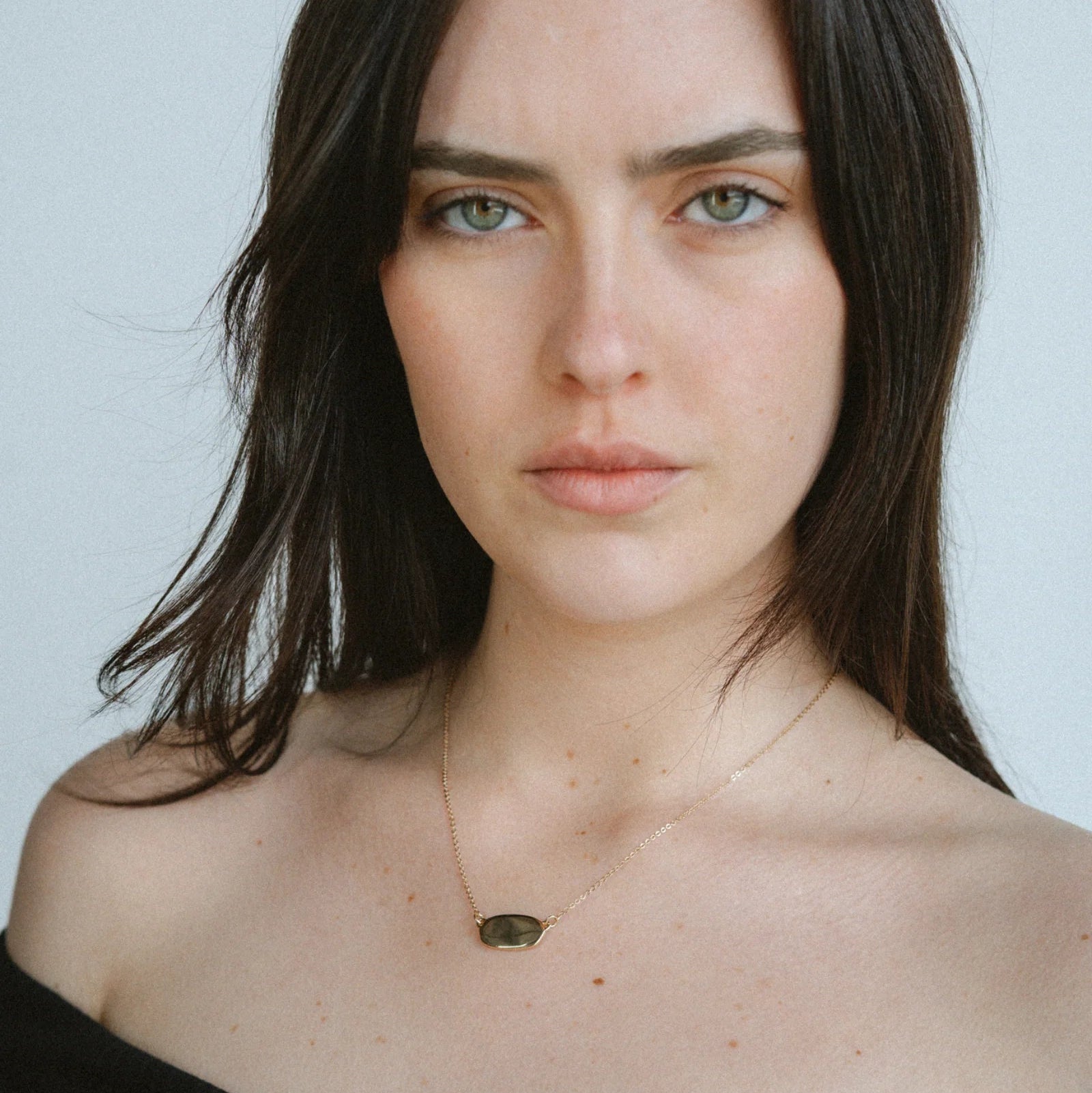 Woman wearing a necklace with a pendant against a plain background