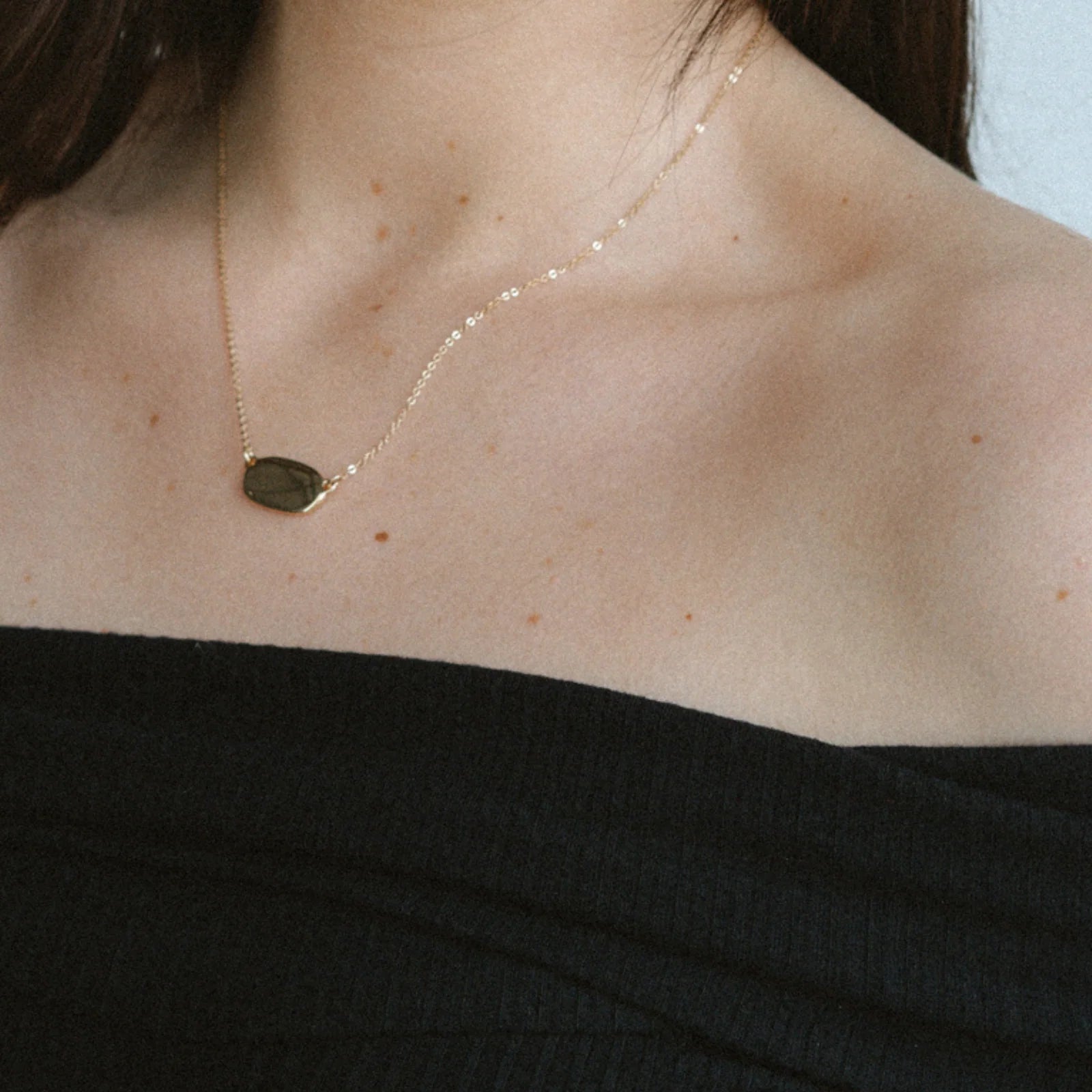 Gold necklace with a pendant on a person wearing a black top.